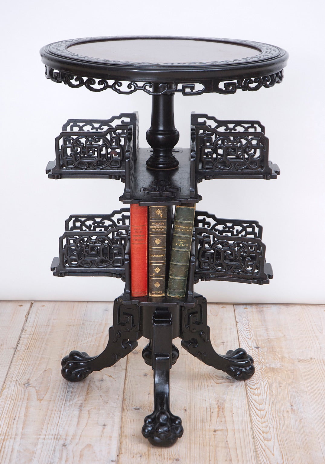 An ebonized Chinese export table with two revolving tiers for books and resting on tripod base with ball-and-claw feet. Round top is inset with stone (light burgundy-colored) with molding around the perimeter depicting a string of carved daisies