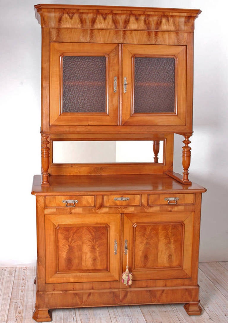 A fine Louis Philippe hutch in French cherry and book matched cherry veneers with glazed upper cupboard resting on turned columns, mirrored back with three silver drawers over paneled cupboard. Textured milk glass was a later addition as are the