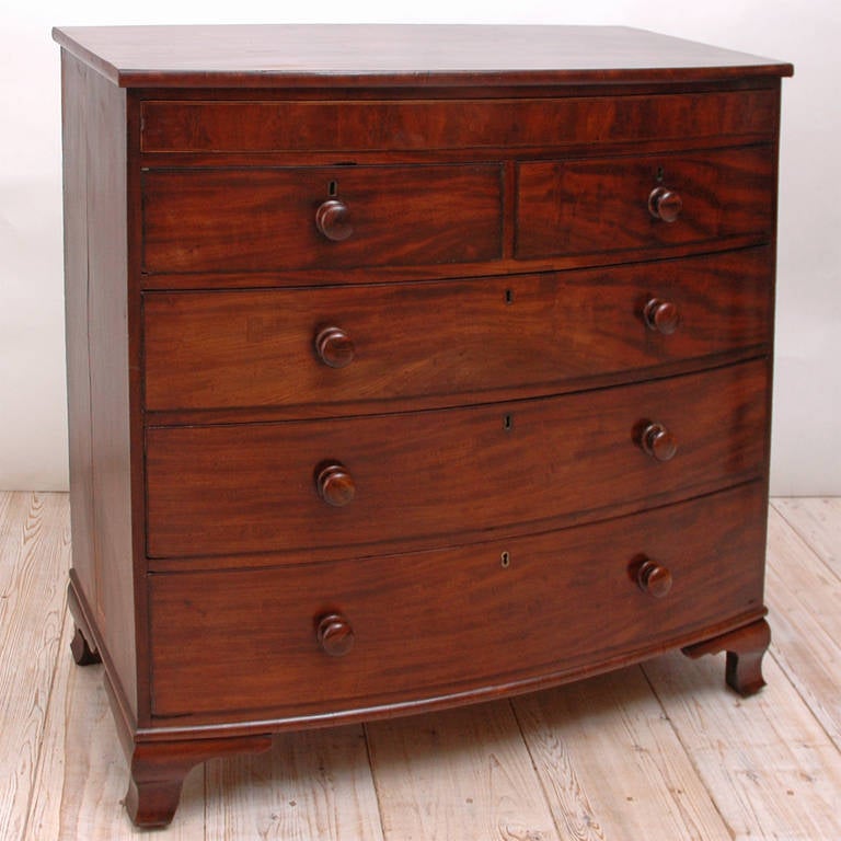 An English bow-front chest in mahogany with ogee bracket foot. Features a secret drawer just below the top, with two drawers over three graduated long drawers. Offers original rosewood pulls and working locks. England, circa 1840. Note: Drawers