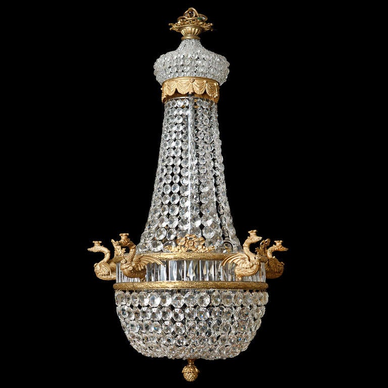 An extremely elegant French Empire revival ormolu and crystal tent form chandelier with swan form candle holders and Neo-Classical motifs c. 1900.
The foliate corona hung with elongated pendants and strings of faceted drops, above a cartouche