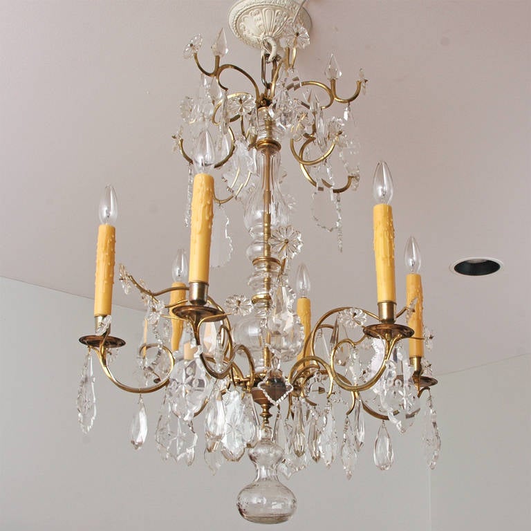 Cast brass and forged armature with handblown glass vase-forms surrounding the structural center of the chandelier. Chandelier is adorned with cut and beveled crystal prisms and terminates with a beautiful handblown solid cut crystal pendant hanging