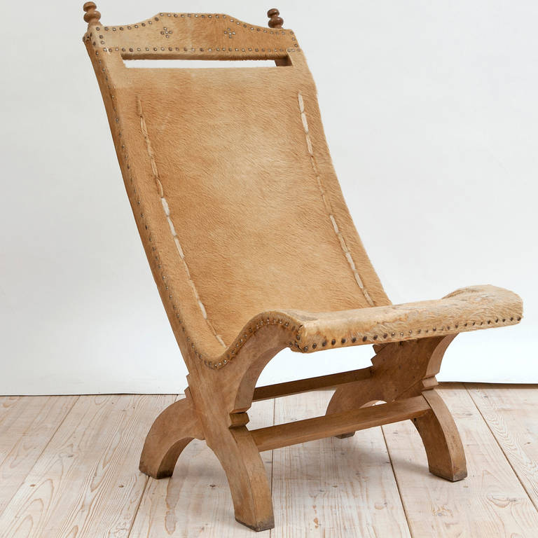 A sturdy vintage reclining chair with cow hide sewn onto the seat and back with decorative nailheads along the upper slat and along the seat, side and back edges.

Measures: 22