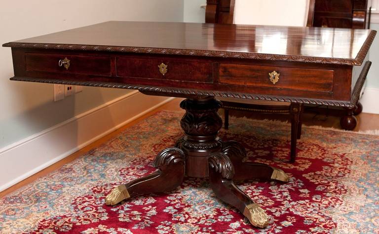 A beautiful Philadelphia partners desk in mahogany with gadrooned top and apron resting on center pedestal with carved baluster and legs, and ending in brass casters with lions' paw feet. Offers a total of four drawers, with two on each side,