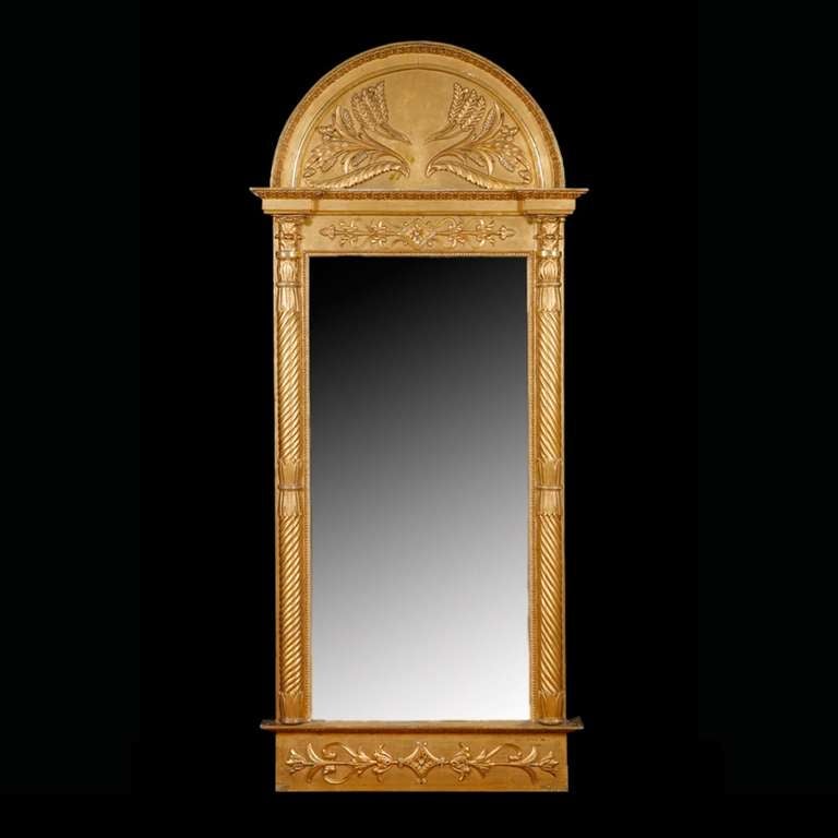 A large and impressive Empire mirror in giltwood from the court of French-born, Swedish king, Carl Johan of the House of Bernadotte. The mirror is flanked by columns with spiraling, and topped with acanthus-carved capitals. Decorative motifs on