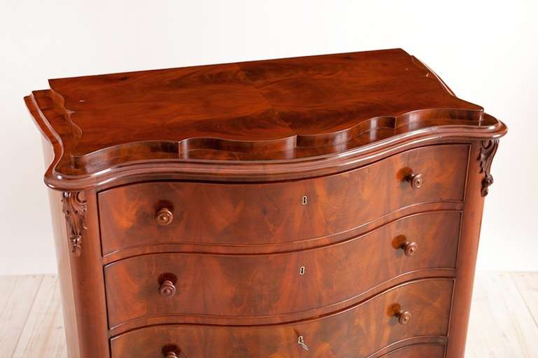 An extraordinary rococo-style chest in mahogany with serpentine front in book-matched figured mahogany showcasing the beautiful grain of the wood. Sweden, circa 1850. Features a scalloped pedestal top, original turned pulls on all four drawers, with