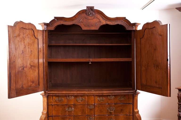 A very fine Dutch Rococo kast or linen press in walnut and burled walnut with inlaid bandings in satinwood and all original brasses. Features an arched cornice with shaped cabinet doors above a serpentine front chest housing two side-by-side drawers