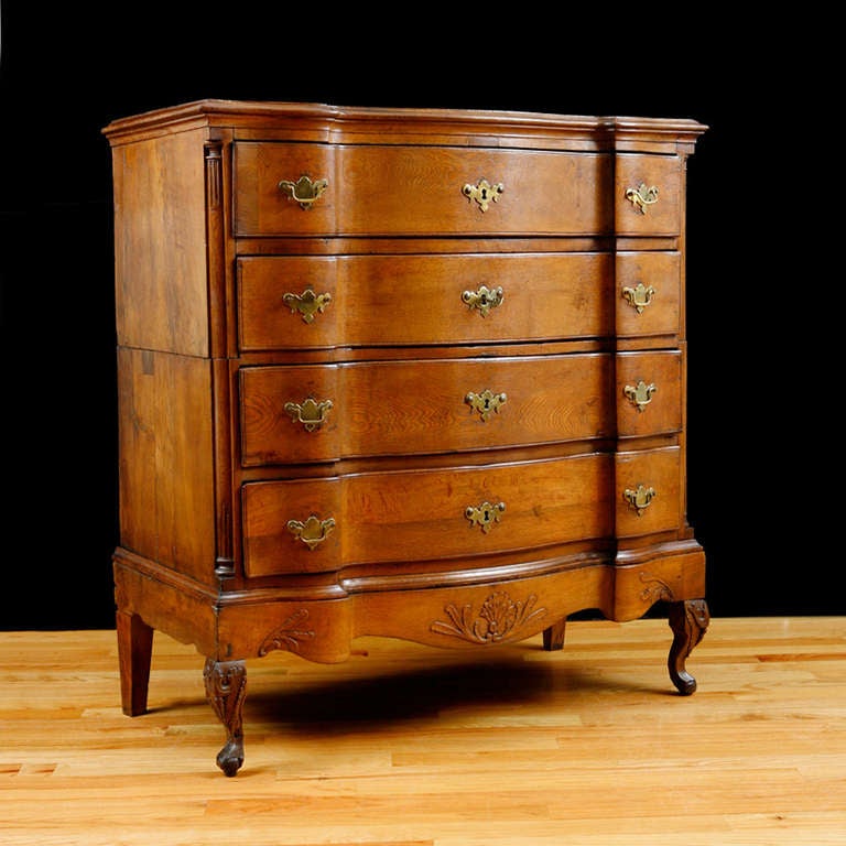 An 18th century baroque chest of drawers with four block front drawers. Chest is in two sections with a floral carving on the plinth base and on the knees of the Queen Anne style feet. Original hardware and quarter columns flanking the