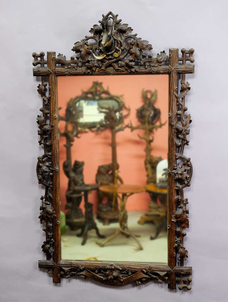a large antique black forest mirror decorated with elaborate foliage carvings and a mass chamois head as well as wild boar tusks on top. germany ca. 1890.