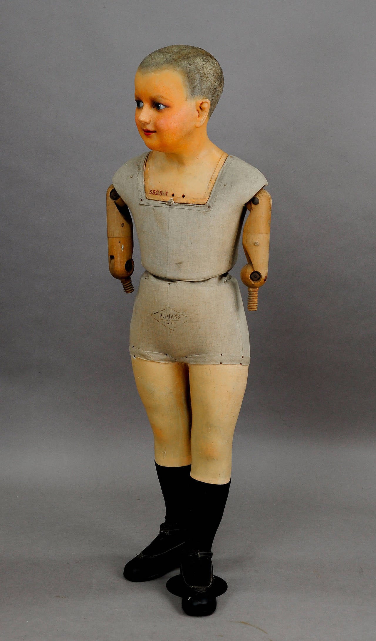 An antique child mannequin by Pierre Imans, Paris. With wax head and glass eyes. Body made of wood, covered with fabric. The arms are made of wood, legs made of plaster. Back and body marked. Executed, circa 1920.