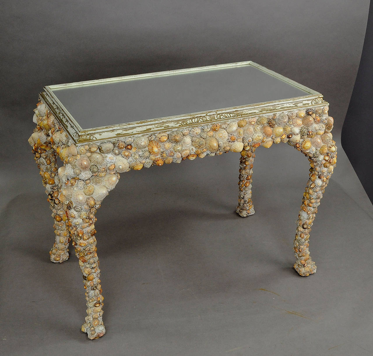 A wonderful coffee table from the 1940s. Made of wood and coated with an abundance of seashells. Wooden ornamented top frame with mirror inset.