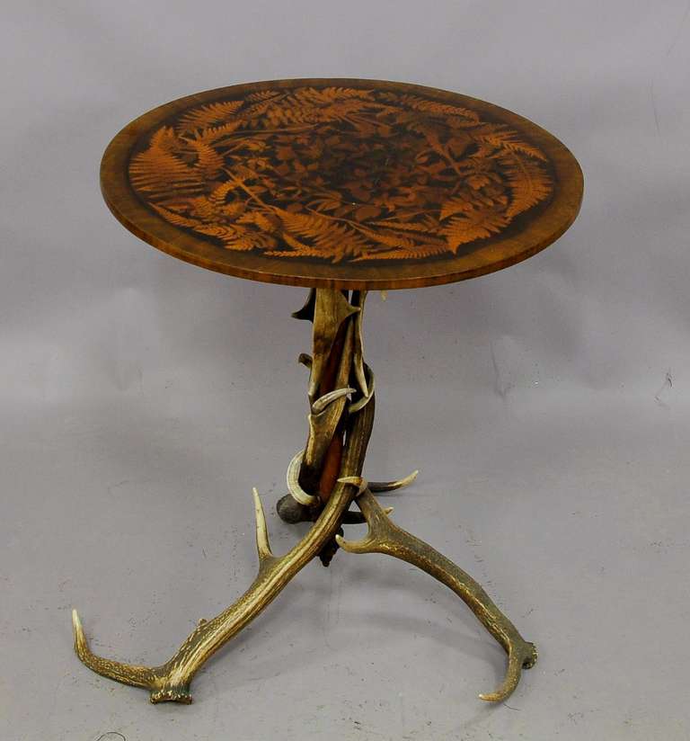 A circular occasional table. Base made with antlers from the stag and fallow deer, wood top with elaborate inlay works depicting several kinds of foliage. Executed circa 1880, Austria.