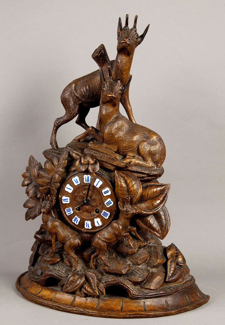 a handcarved mantel clock, depicting a family of four chamois resting on a rocky outcrop. executed ca. 1900.