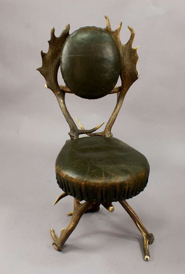 an antique black forest antler parlor chair with fallow deer backrests. original green leather cover. executed ca. 1860.