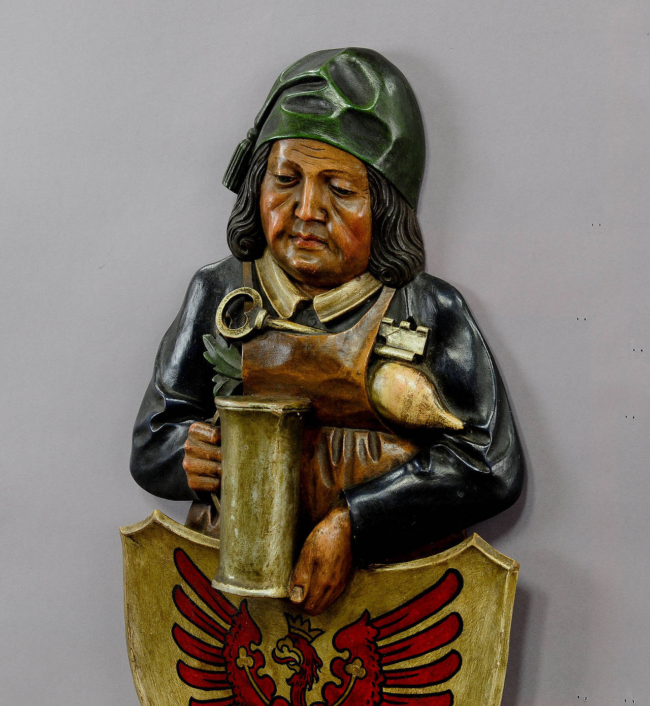 A great hand-carved and painted wall plaque of a cellarer holding a beer mug, gilded shield with red eagle, the heraldig crest of the state Brandenburg in Germany, executed circa 1920.