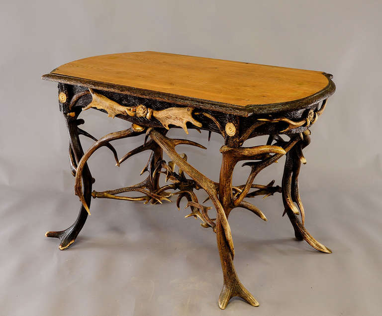 an antique antler table or desk. decorated with several antlers from the deer, fallow deer and virginia deer. each corner with turned horn ends and each side with wild boar tusks and figural handcarved horn roses. wooden top with carved border.