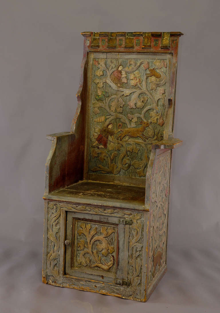 An antique oakwood throne, painted and carved with stylized flower tendrils, human and animal figures. Underneath the seat a small cupboard. Executed, circa 1920.