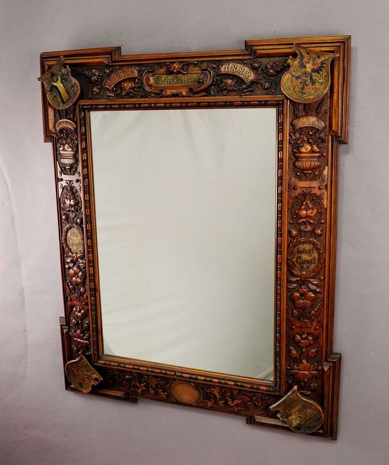 a large mirror with a finely carved frame from partenkirchen, bavaria 1888. on the edges 4 carved blazons showing the city coat of arms of partenkirchen and bavaria. frame with inscription: 