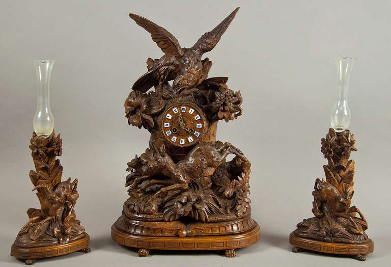 a handcarved wood mantle clock with two side vases. an eagle is sitting on a tree trunk, with a chamois at his feet. the two side pieces show a chamois and an ibex. a very detailed carving.
swiss brienz ca. 1900.