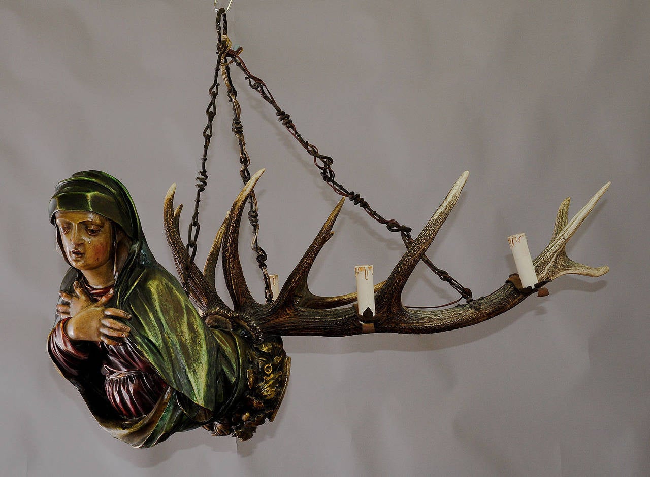 an antique black forest antler chandelier - named lusterweibchen or lüsterweibchen. a wooden carved praying madonna in gothical style, blazon with bavarian emblem. attached a pair of original stag antlers. executed ca. 1900 in Germany. (height