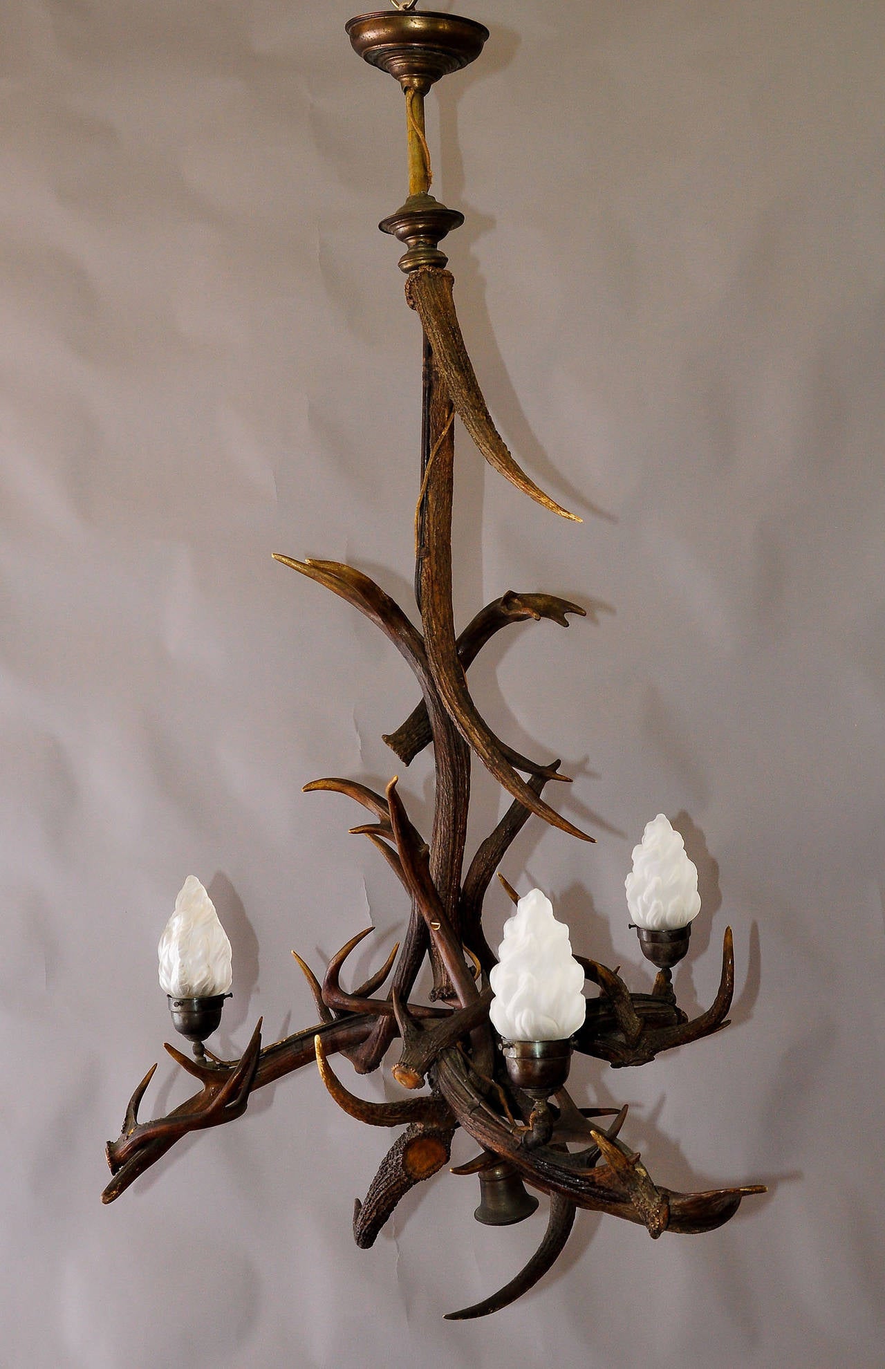 A large chandelier made of several stag and Virginia deer antlers, with four spouts and three glass shades in the design of flames. Manufactured circa 1930. Originally for gas. Later electrified.