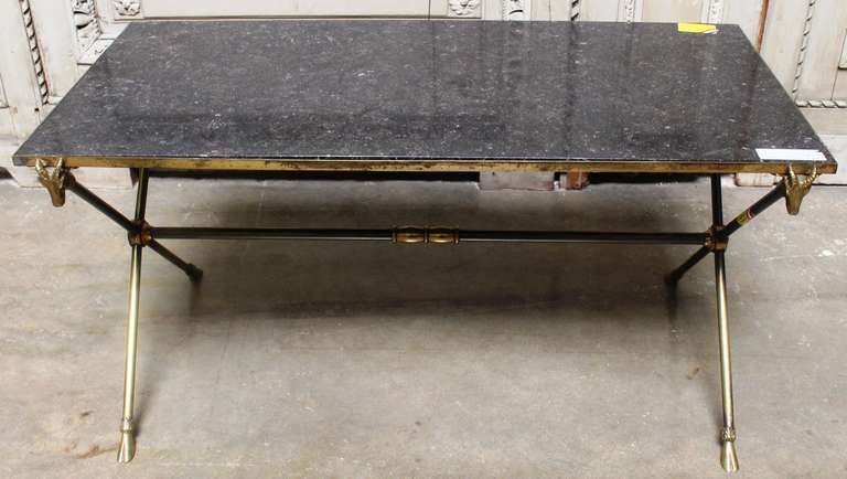 A bronze Maison Ramsay cocktail table with ram heads motif and grey limestone top. The table has an old patina and some old silver metal plating that has mostly been rubbed off over the years.