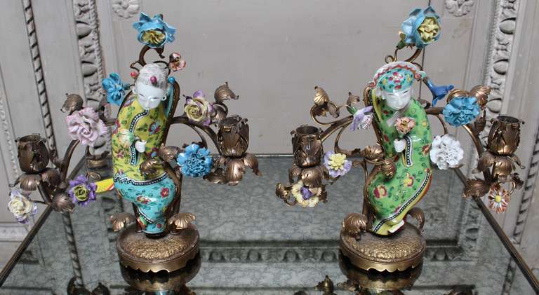 A pair of bronze and porcelain girandoles depicting two Chinese figures in dance, surrounded by French cast bronze and porcelain flowers. This pair of candle holders could be wired for lamps or for candles. The are ideal for mantel decorations.