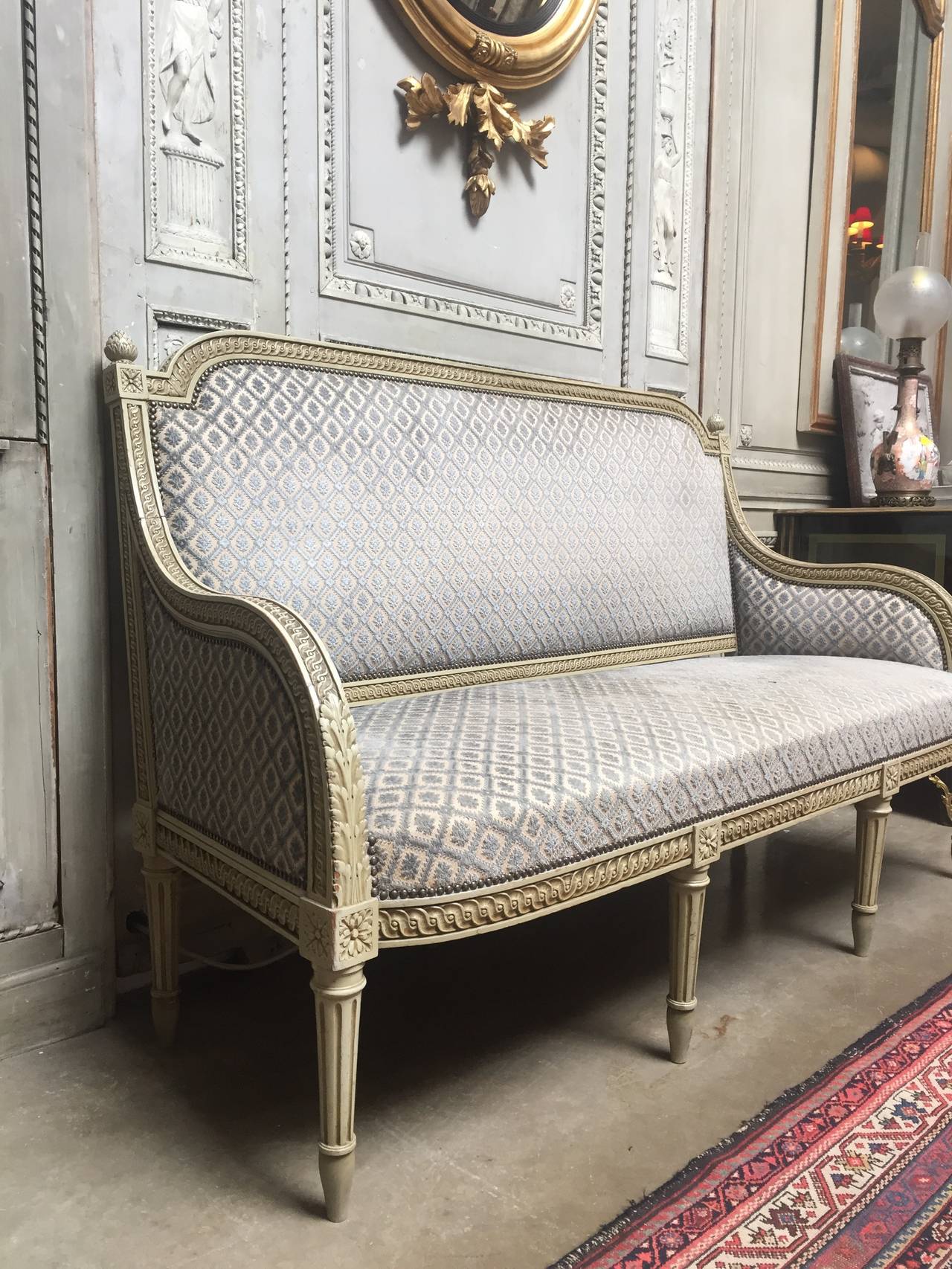 A French Louis XVI style nicely carved canape, sofa with gadrooning, acanthus leaves and acorn finials on fluted legs. This early 20th century sofa is deep and sits higher than most antiques. It has a gray green old painted finish and is ready for
