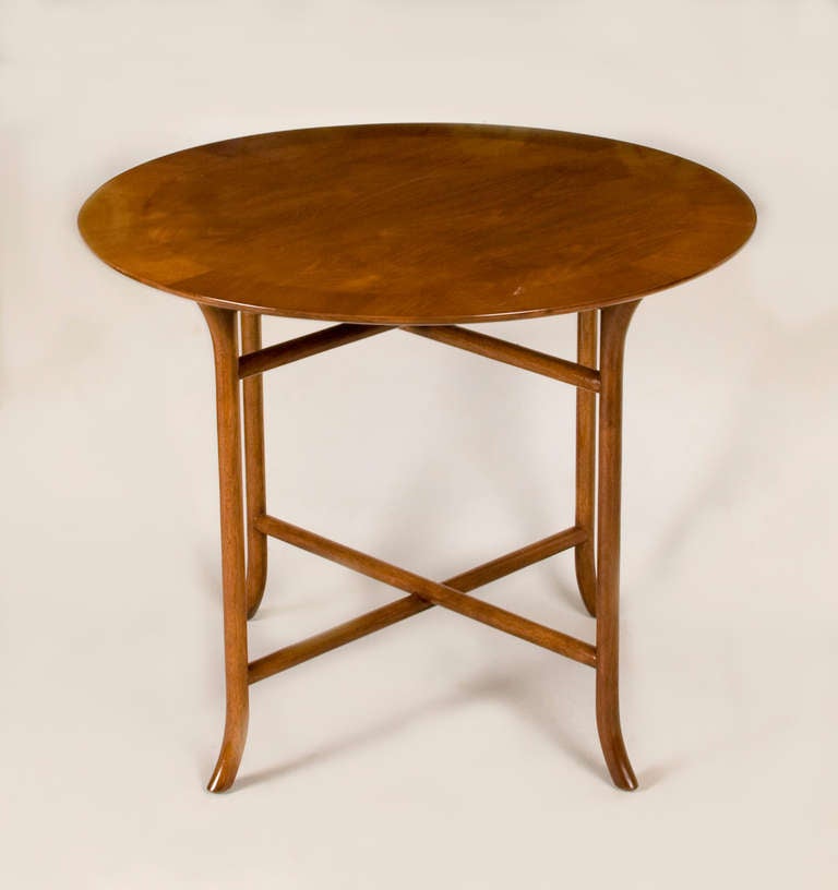 Classically designed rare circular occasional table by T.H. Robsjohn Gibbings for Widdicomb, Model #3336. Exquisitely crafted walnut veneered band top with a round beveled edge to underside. Pair of turned cross stretchers along sculpted legs with