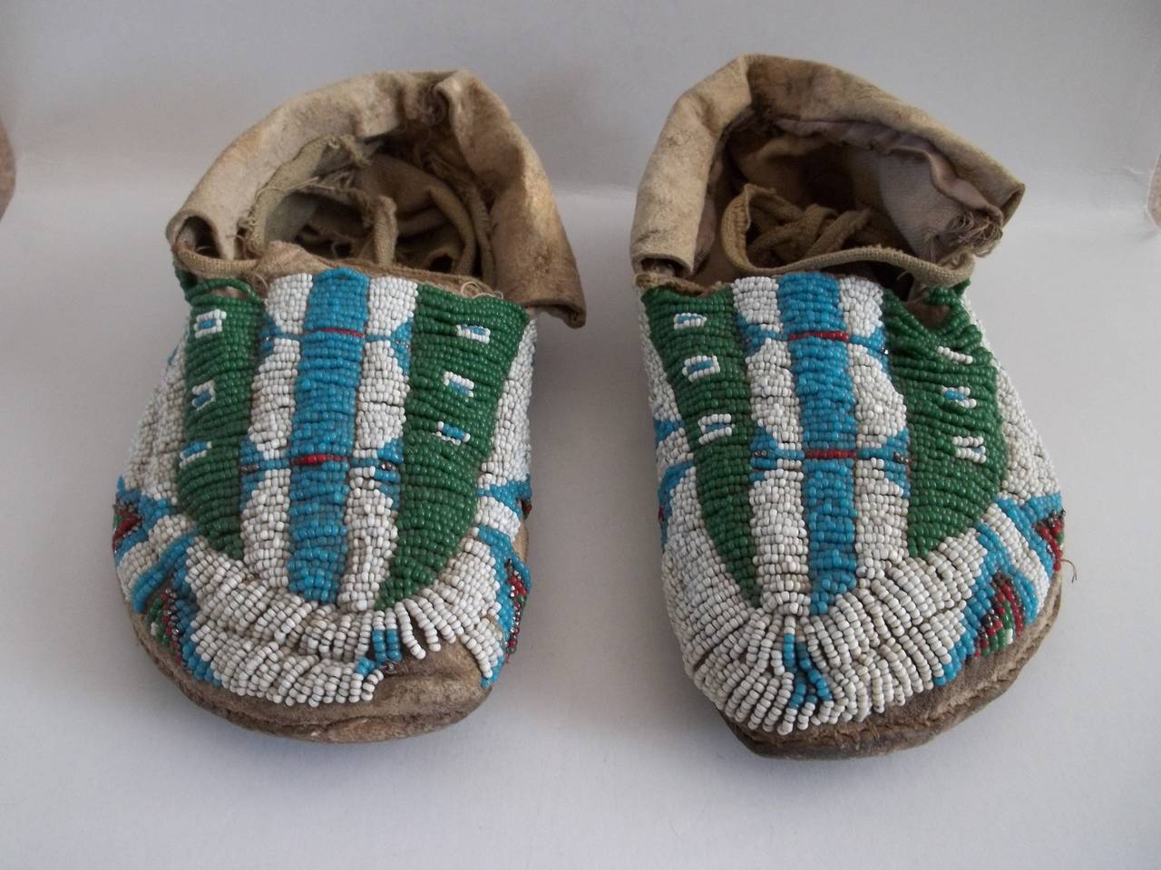 This is a rare pair of North American Central Plains beaded hide moccasins.

The uppers are fully beaded in a geometric pattern, using white
red, green and blue hand stitched beads.

We date them to the mid-19th century or possibly earlier.