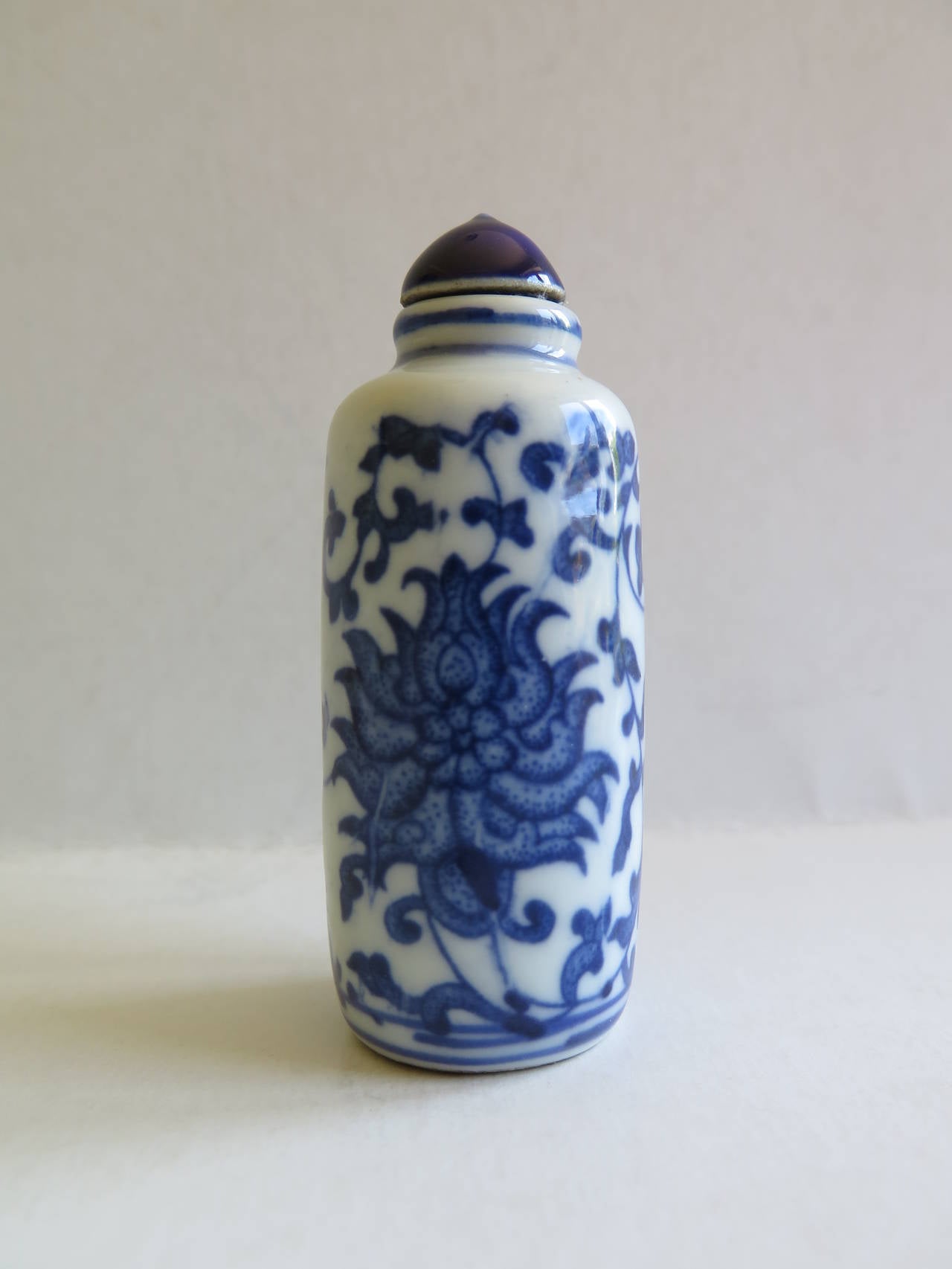 This is a good quality Chinese Snuff Bottle, made from porcelain, circa 1930.

The cylindrical bottle is decorated in varying shades of under-glaze blue, having a large central peony to either side with trailing lotus scrolls linking to the