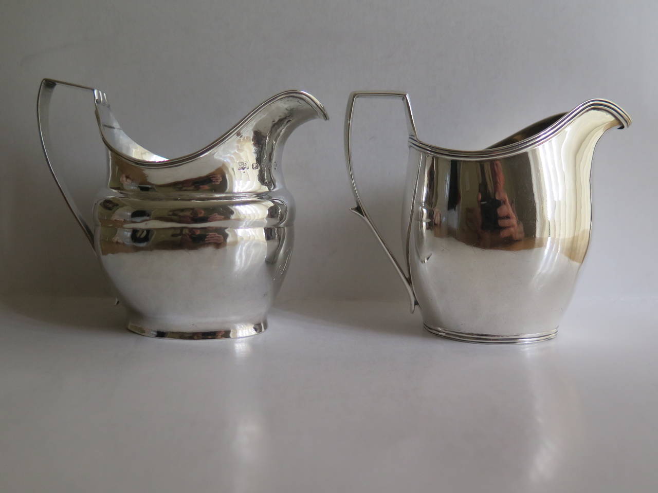 These are TWO different Sterling Silver, English, Cream Jugs from the George III period, very early in the 19th Century.

Both jugs are classic vase shaped with a high loop handle, reeded rim and are fully hall marked. They have a liquid volume of