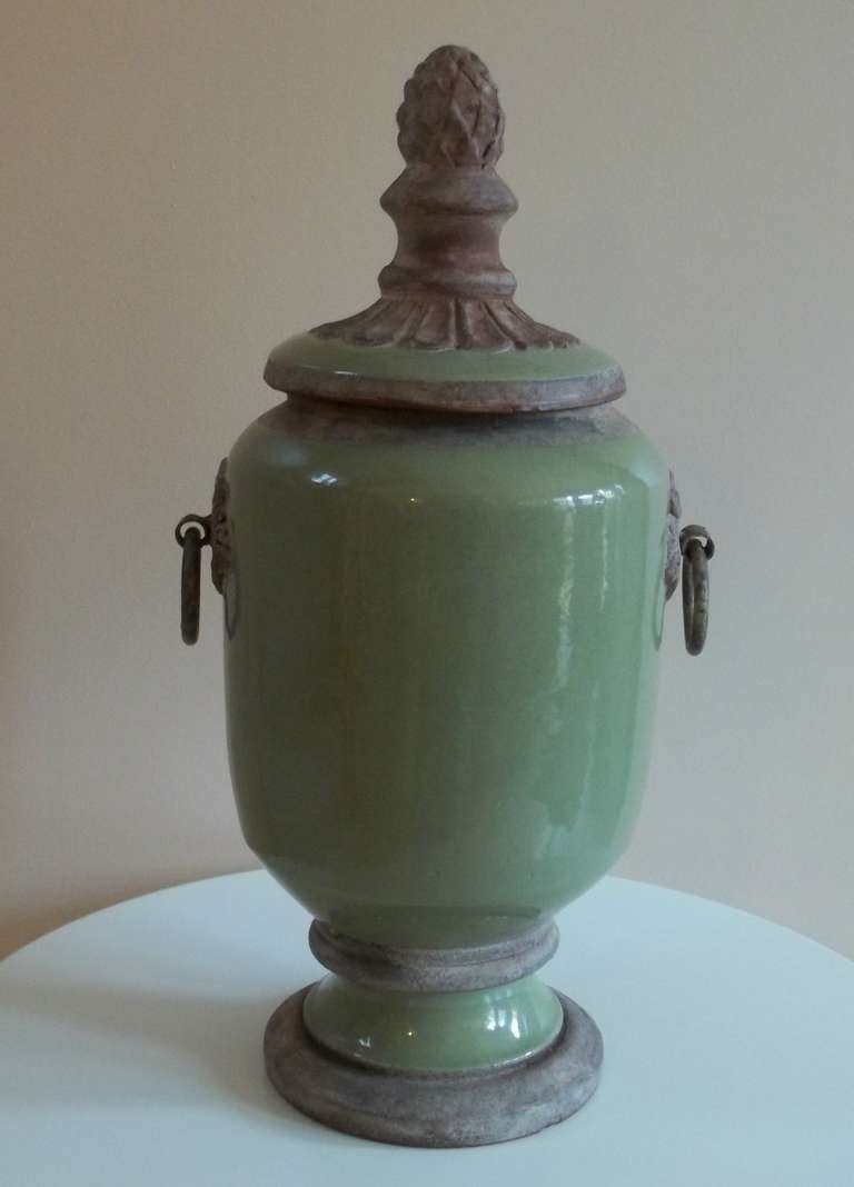 This is an unusual Stoneware Lidded Jar.

The jar is partially glazed in a soft apple green colour and has two side mouldings  with two circular metal (bronze) handles, one either side.

The lid is also partially glazed and has a good finial /