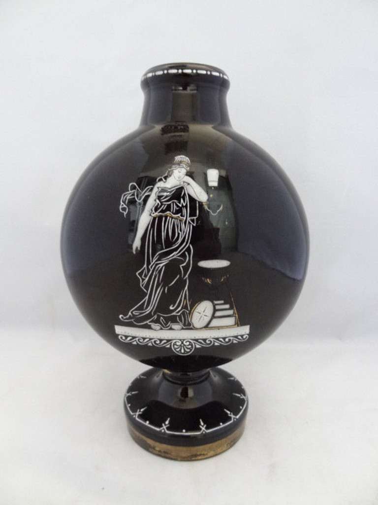 Staffordshire black glass footed moon flask with white enamelling frieze around neck and white enamelling and gilt decoration around the foot. The front shows a Grecian maiden beside an urn, depicted in white enamel with gilt highlights. The back