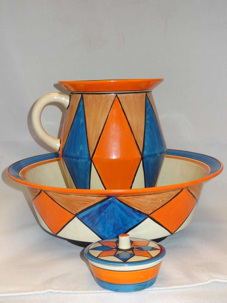 Unusual bowl, pitcher and lidded soap dish pieces by Clarice Cliff, decorated with a striking design of orange and blue triangles and diamonds in the 'Original Bizarre' pattern. 

Dimensions: 

Bowl 12.00 cm. h x 36.40 cm. d 

Jug 23.40 cm. h