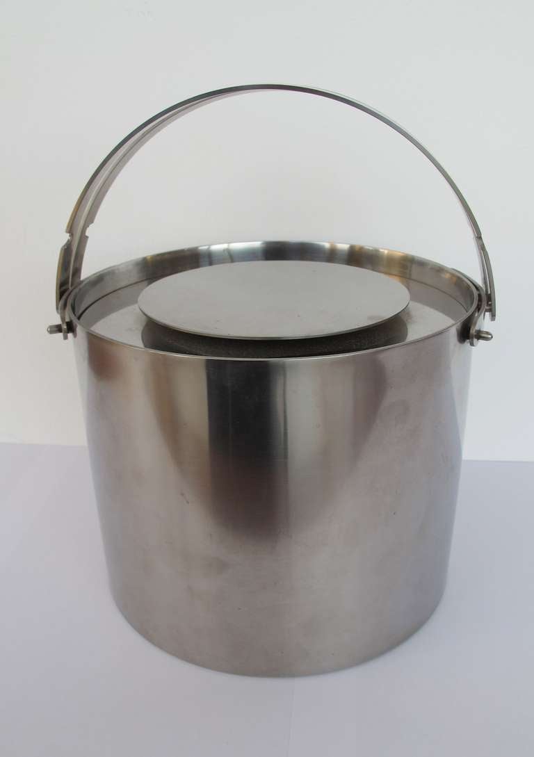 Stainless steel ice bucket by Arne Jacobsen for Stelton with modern functional design. It has folding handles and a double-walled stainless steel construction which helps keep the ice cool. This ice bucket is part of the Cylinda collection, launched