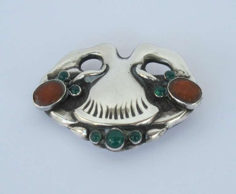 Elegant silver brooch modelled as a stylised flower with inlaid gemstones. There are two amber gems and three chrysoprase cabochons. Fine jewelry with the Maker's mark of Georg Jensen, 1909-1914.