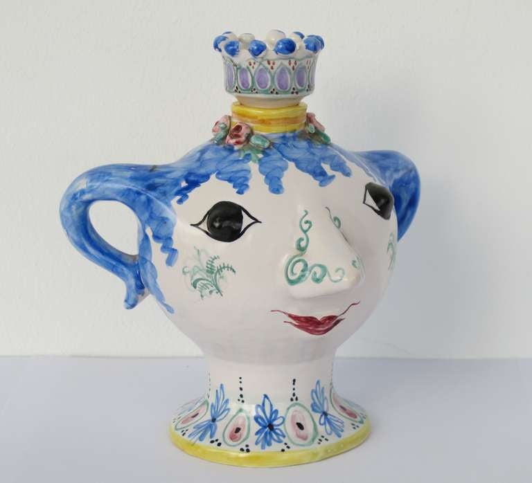 Handpainted ceramic bottle in the shape of a female head. The cork has the shape of a crown and can be taken off. The round faced head with distinctive decorative floral motifs on the nose, cheeks and along the foot is an early design by  Bjørn