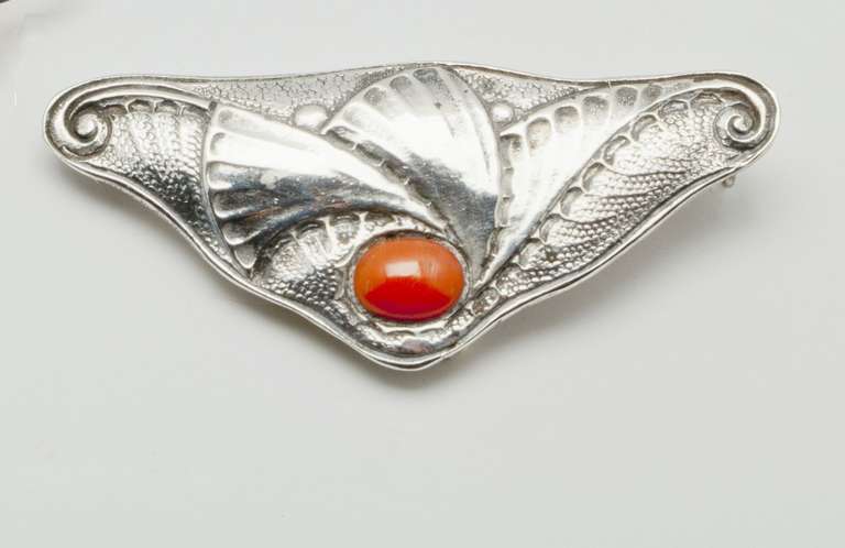 This elegant silver broche with red coral stone is made by the famous Dutch goldsmith Fons Reggers in the Amsterdam School style during the 1920s. 

The firm Gebr. Reggers was founded in 1919 by two brothers Fons and Rein Reggers who came from a