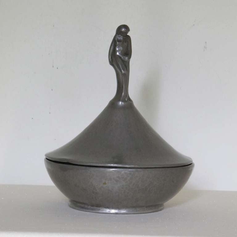 This hammered tin pot has an elegant stylized female figure on top of the lid. It was made by Cris Agterberg during the 1920's-1930s and it has a signature stamp on the bottom (see image). 

Cris Agterberg (1883-1948) was a Dutch designer and