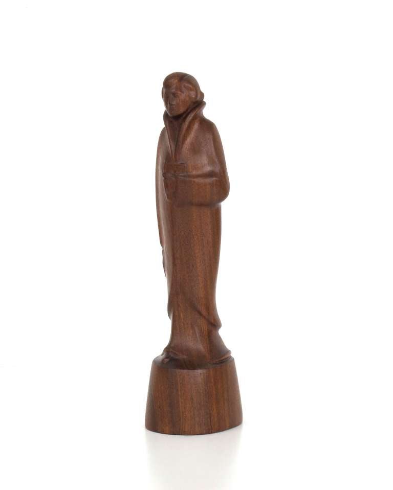 1920s teak sculpture of a walking female figure with long garment holding a handbag in her right hand and a book in her left hand. The monogram of the artist Leendert Verstoep is carved into the basement (see image). 

The sculpture probably depicts