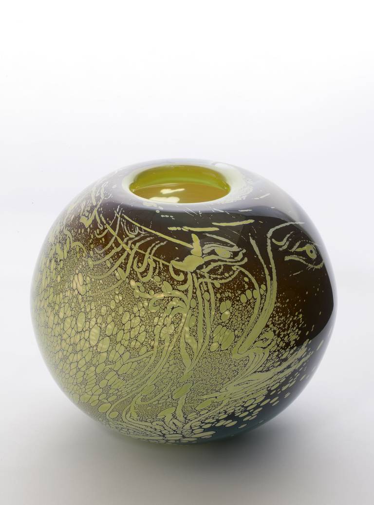Round shaped art glass vase with human face by Dutch glass artist Willem Heesen. The green and brown glass object is freely shaped and has a diamond-incised signature on the bottom. On one side it has a pattern of transparent flecks that reminds of