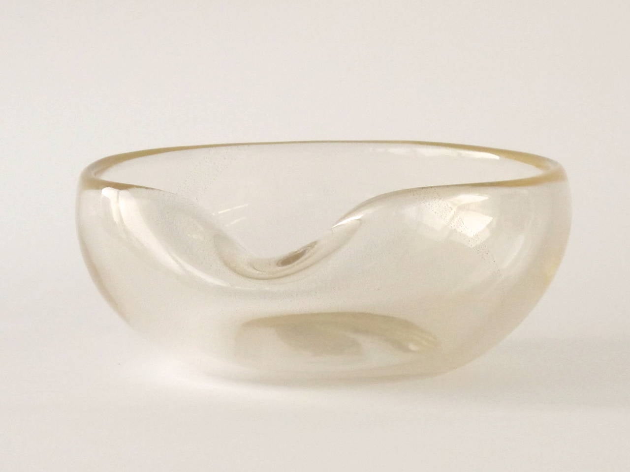 This unique transparent bowl by Archimede Seguso is enriched with gold flecks, giving the object a fascinating appearance. Venetian Archimede Seguso (1909-1999) was a Murano glass Maestro. 

The round shape of the bowl is interrupted by a dent.