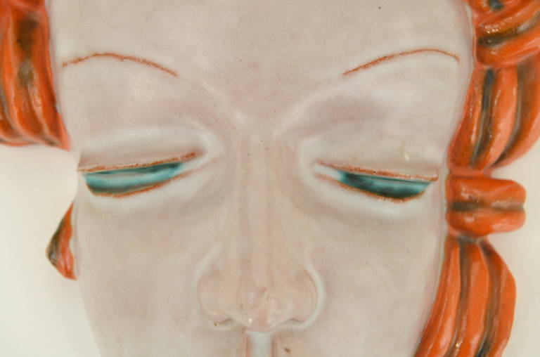 Ceramic wall mask designed by Rudolf Knörlein. This expressive work is an perfect example of Knörlein’s typical style with a pale woman's face in combination with red hair.  It was manufactured around 1931 by the Viennese Goldscheider factory and it
