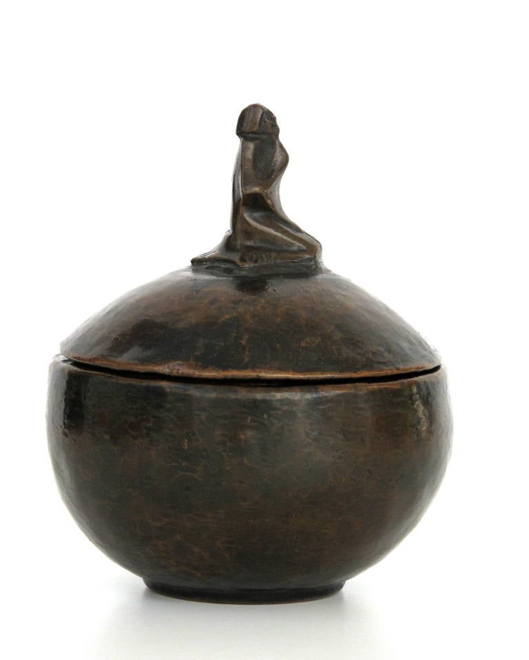 This hammered red copper pot has an elegant stylized figure on top of the lid. The kneeling figure had adopted a meditative pose. It was a special piece not only designed by Cris Agterberg but probably also made by him regarding the craftsmanship.