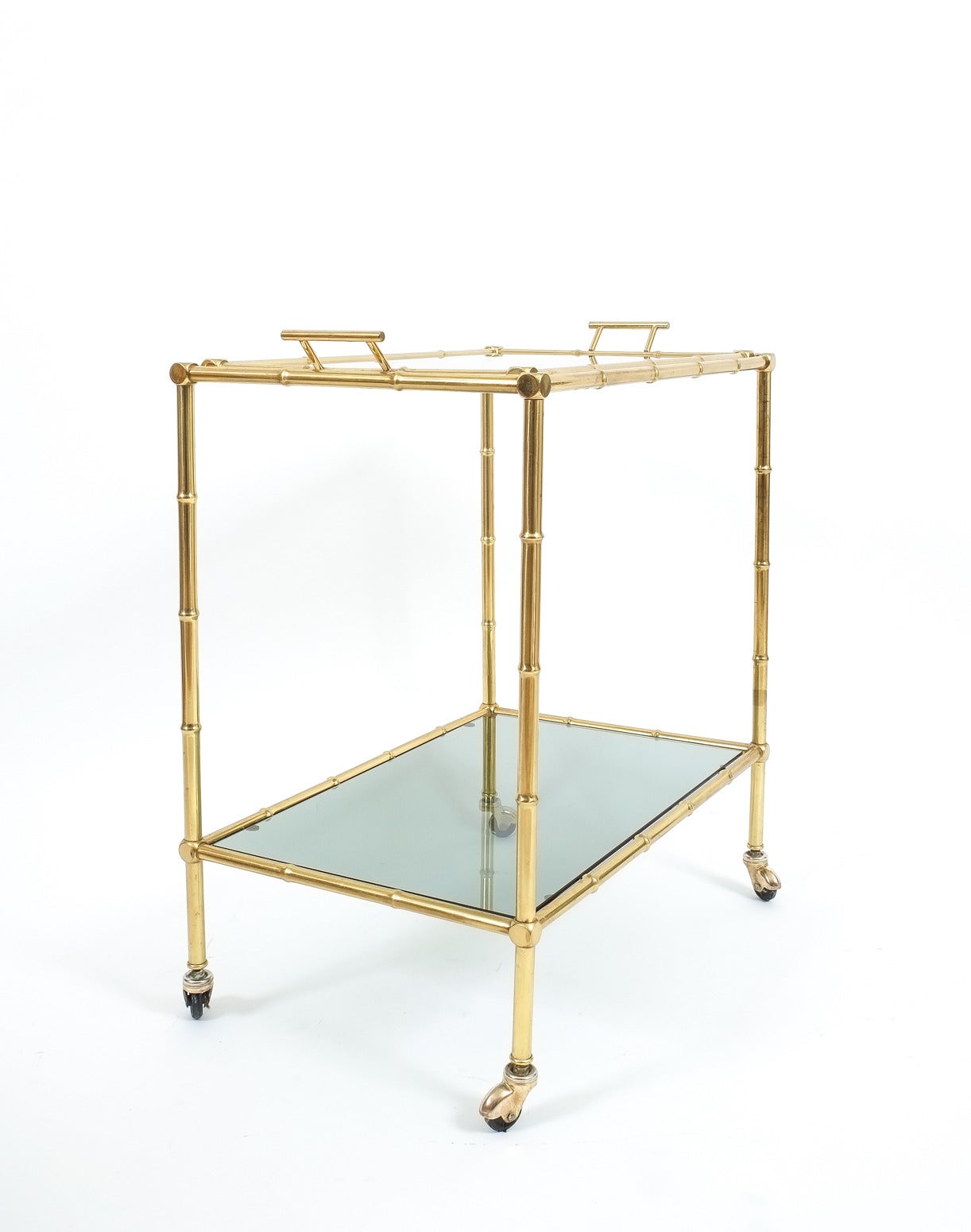 Elegant mid-century liquor or bar cart from France in the tradition of maison Bagues with a removable glass tray and abstracted faux bamboo brass hardware. it's in very good condition.