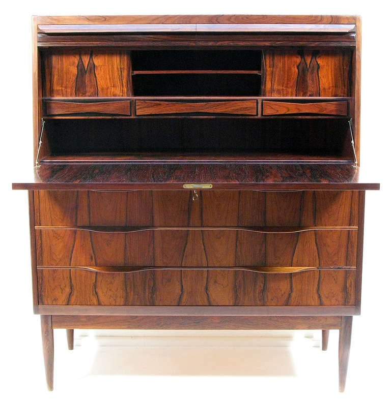 Width: 104cm
Height: 121cm
Depth: 48cm

A beautifully crafted 1960s bureau in solid rosewood by Danish designer Ib Kofod Larsen.

With tapered legs and sculpted handles this bureau features eight beautifully stylized drawers and four useful