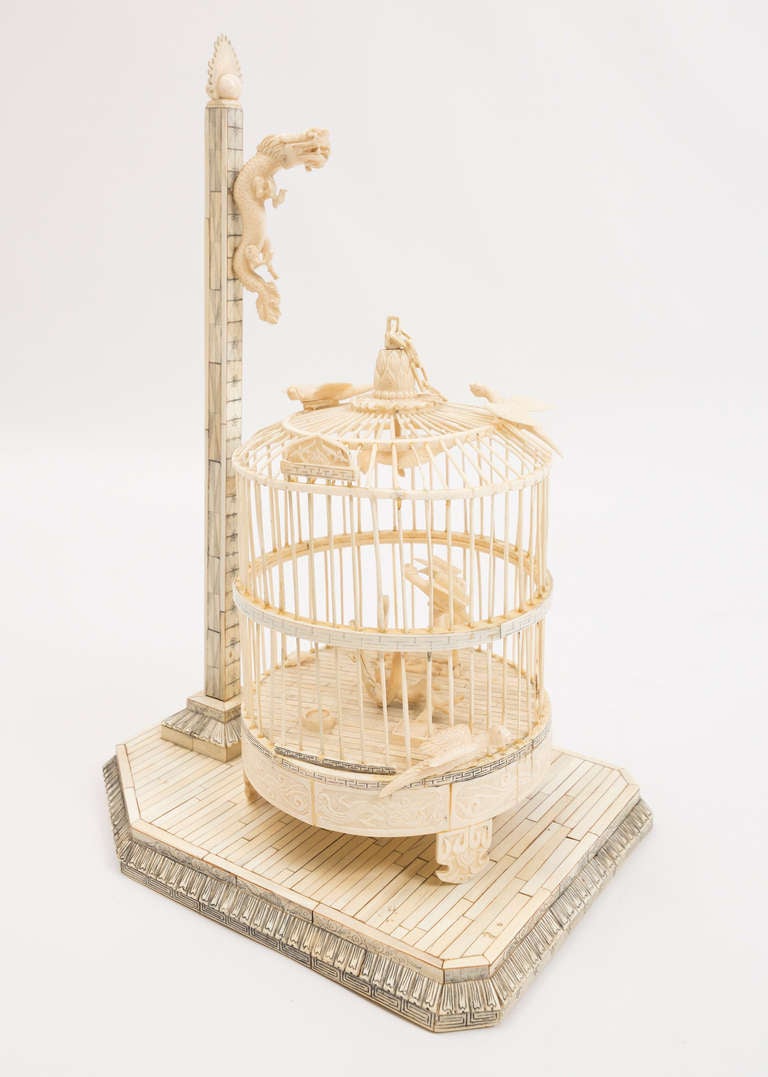 Hand carved ivory birdcage on an ivory stand.  Two birds on the inside, two birds on the top and one bird on the bottom edge.  A dragon is mounted on the vertical bar.  The tongue holds up the birdcage.
