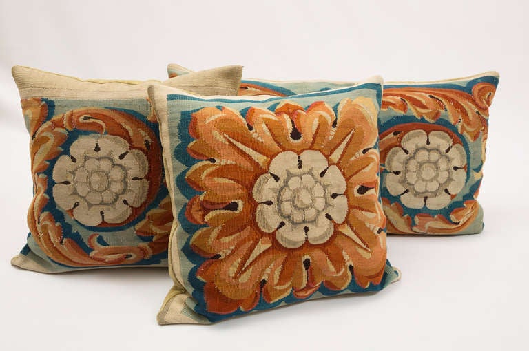 French tapestry fragments made into three pillow with a velvet back. Colors are dark and light blue teal and shades of orange with light gray rosettes.