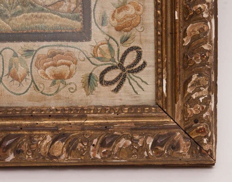 Framed needlework picture of man and a bird with floral border and gold distressed frame.