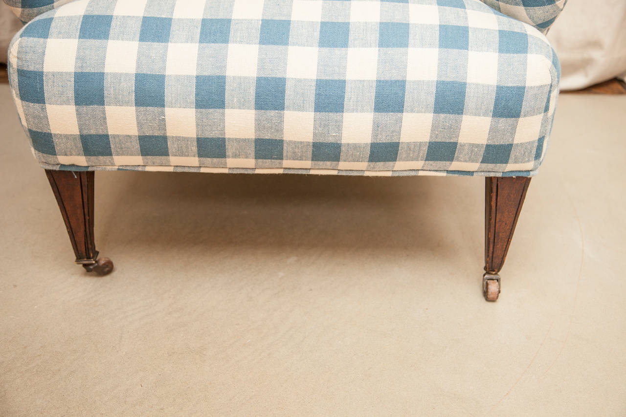 Winged arm chair, mahogany legs with casters. Blue plaid upholstery.